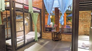 A room with a bunk bed, a small table with a vase, and a window with curtains.