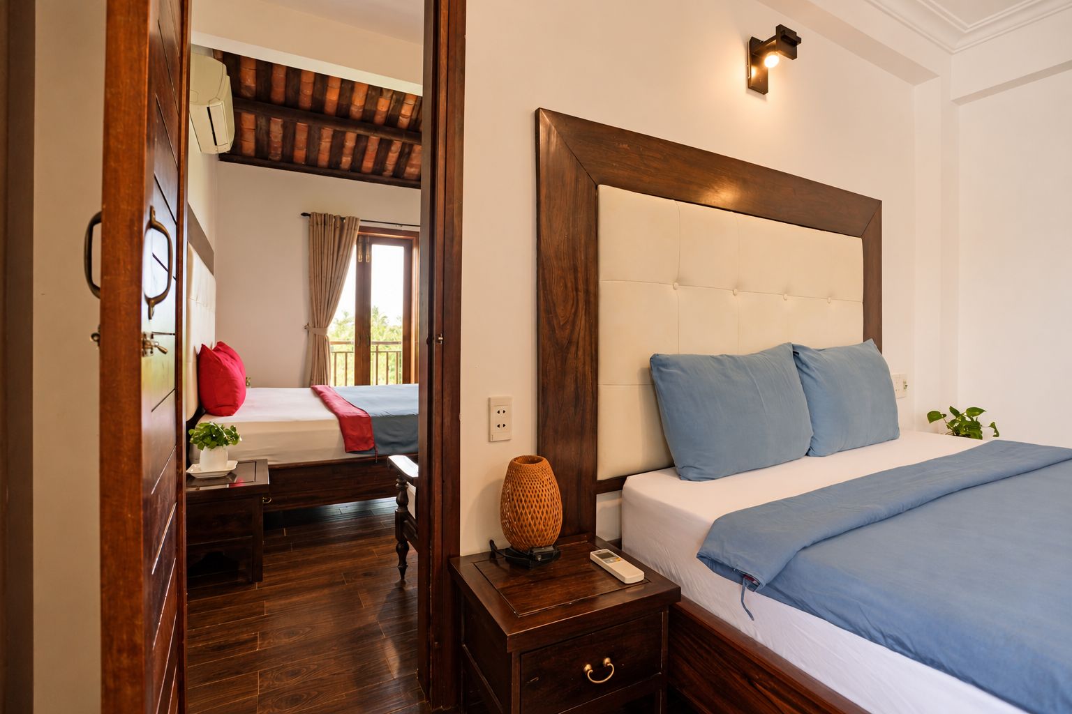 Quarto de hotel com uma cama grande, mesa de cabeceira com abajur e piso de madeira.