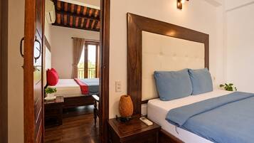 Quarto de hotel com uma cama grande, mesa de cabeceira com abajur e piso de madeira.