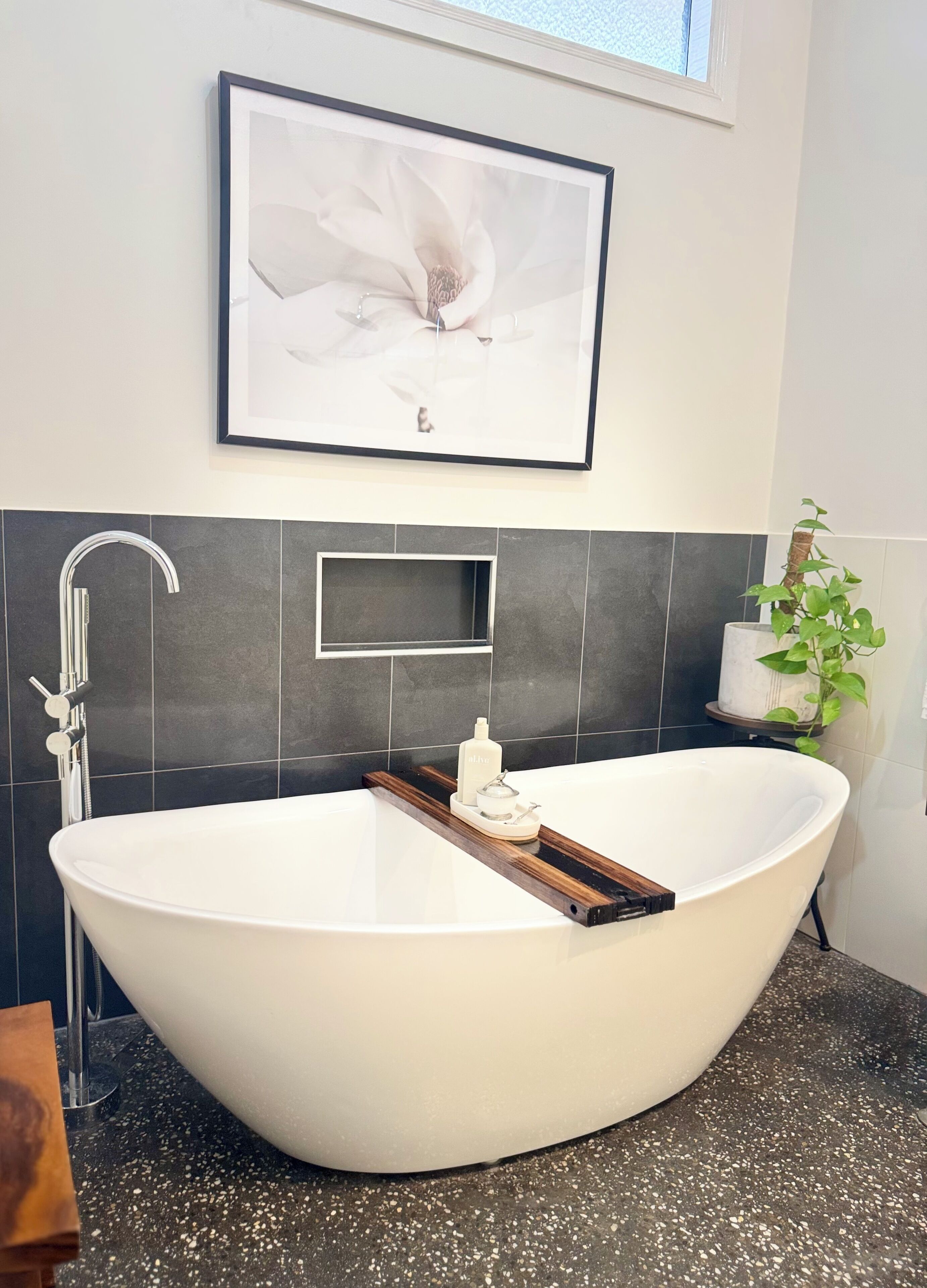 Een moderne badkamer met een vrijstaand bad, een ingelijst beeld erboven en een potplant aan de rechterkant.