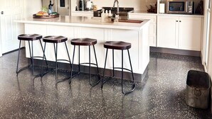 Una cocina moderna con armarios blancos, una isla central con taburetes, electrodomésticos de acero inoxidable e iluminación colgante.