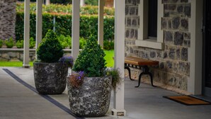 Un porche cubierto con columnas de piedra, un banco y macetas con plantas.