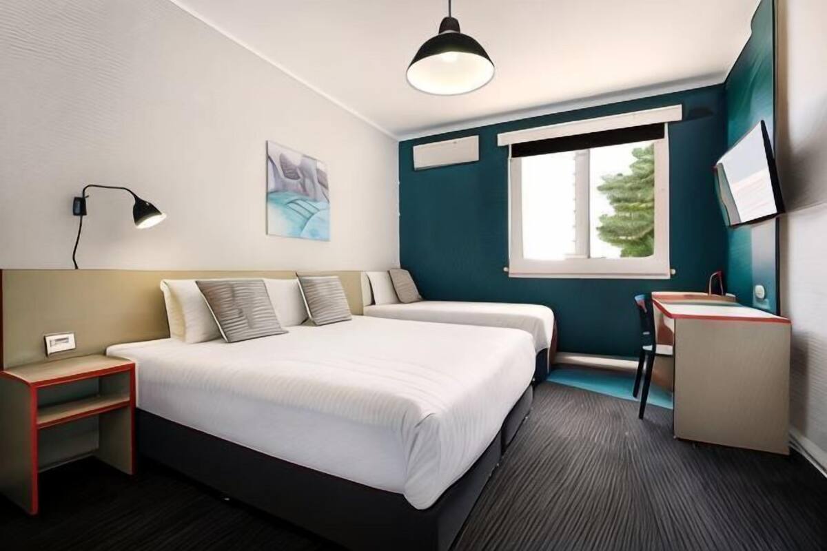 Habitación de hotel con cama, dos mesitas de noche, un escritorio, una silla, televisor y ventana.