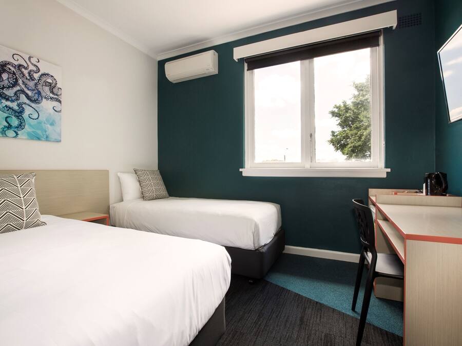 Habitación de hotel con dos camas, un escritorio, una silla, una ventana con vistas y un aire acondicionado de pared.