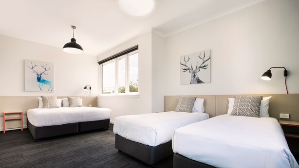 A hotel room with two single beds, a small table, and artwork on the walls. - Greenacre Hotel (Greenacre)