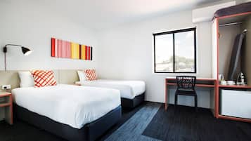 A hotel room with two beds, a desk, a chair, a large window, and a mirror.