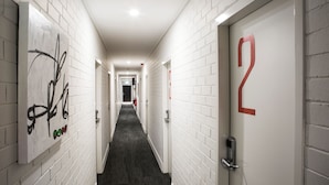 A hallway with white brick walls, numbered doors, and a dark carpet. - Villawood Hotel (Villawood)