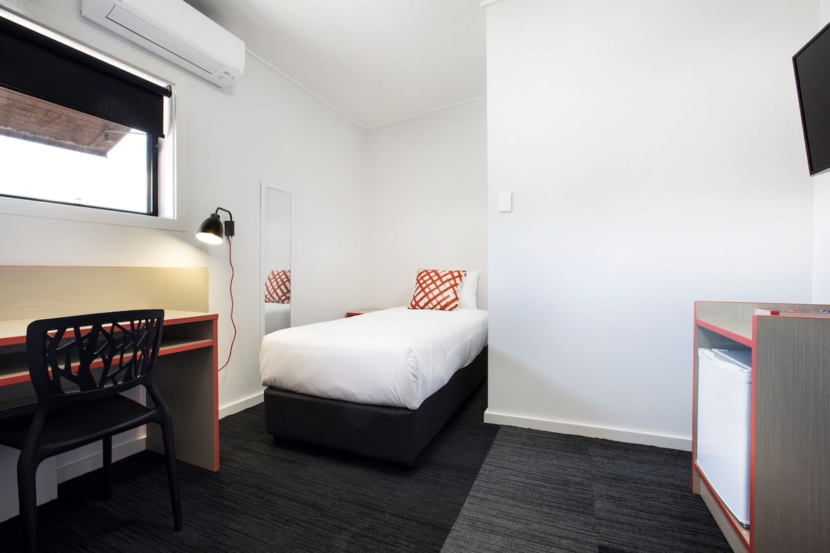 Habitación de hotel pequeña con cama, escritorio, silla, una mesita y televisor montado en la pared.