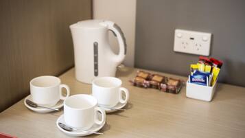 Una mesa con tres tazas y platillos blancos, una tetera eléctrica blanca, una caja de galletas y una caja de pañuelos.
