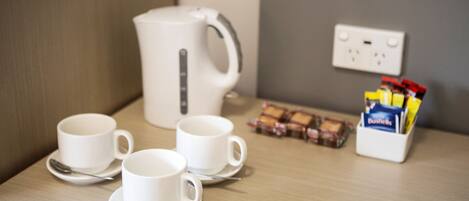 A table with three white cups and saucers, a white electric kettle, a box of biscuits, and a box of tissues.