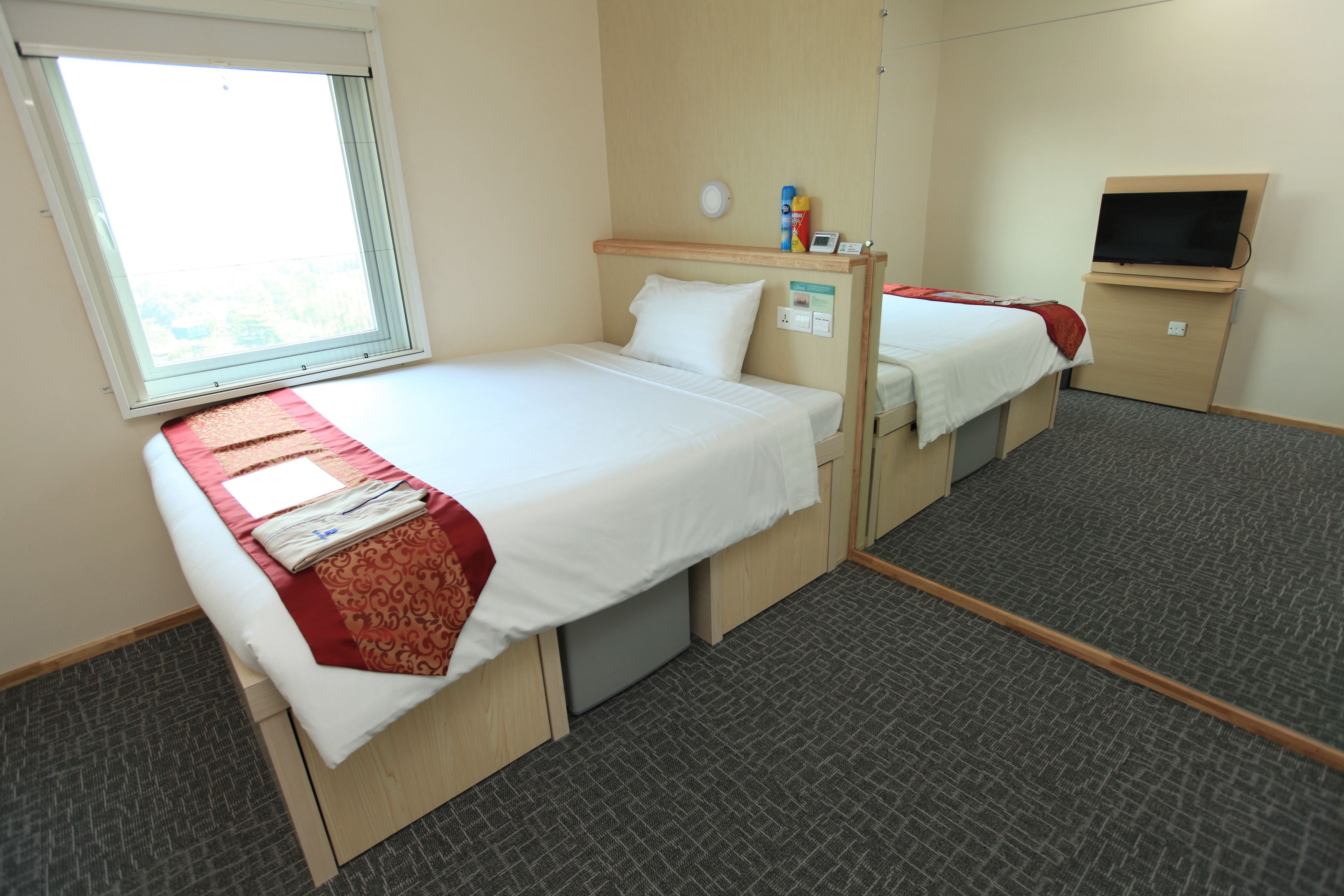 A hotel room with two single beds, a window, a TV, and a small desk.