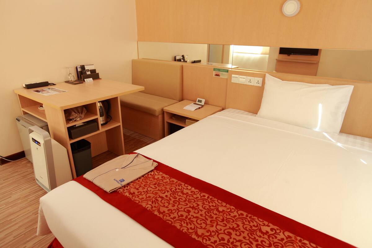 Ein Hotelzimmer mit Bett, Schreibtisch, Stuhl, kleinem Tisch und Mülleimer.