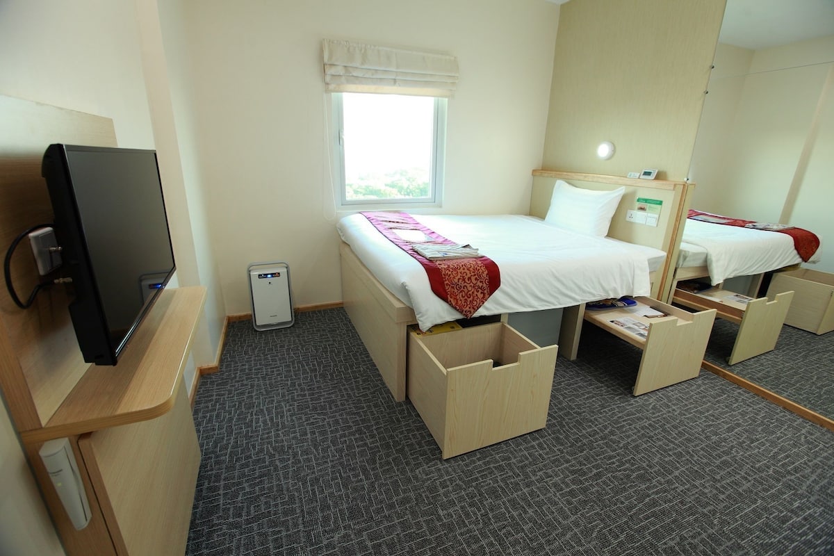 Ein Hotelzimmer mit Bett, Schreibtisch, Computer, Fenster und Spiegel.