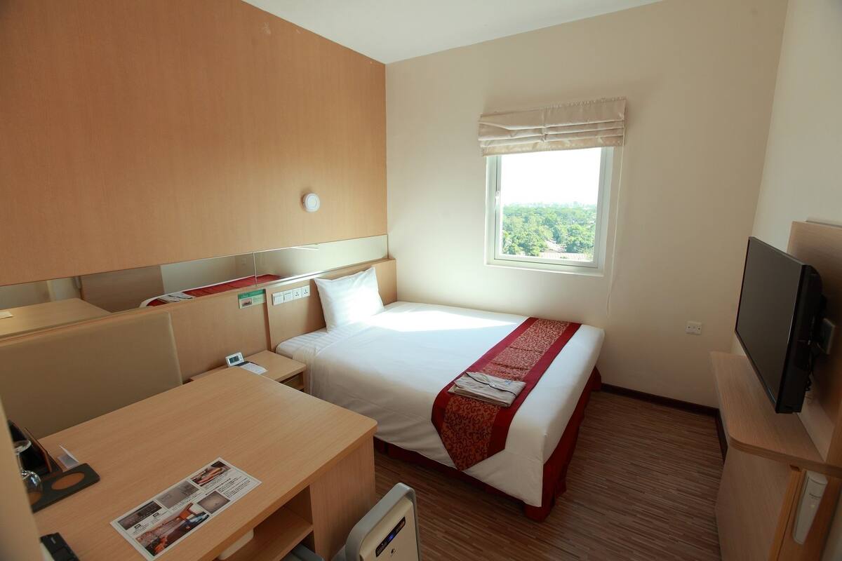 Ein Hotelzimmer mit Bett, Schreibtisch, Fernseher, Fenster mit Blick und Nachttisch.