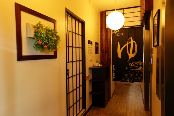 Un pasillo con piso de madera, una planta colgante, una puerta tradicional japonesa estilo shoji y una pared con un letrero decorativo.