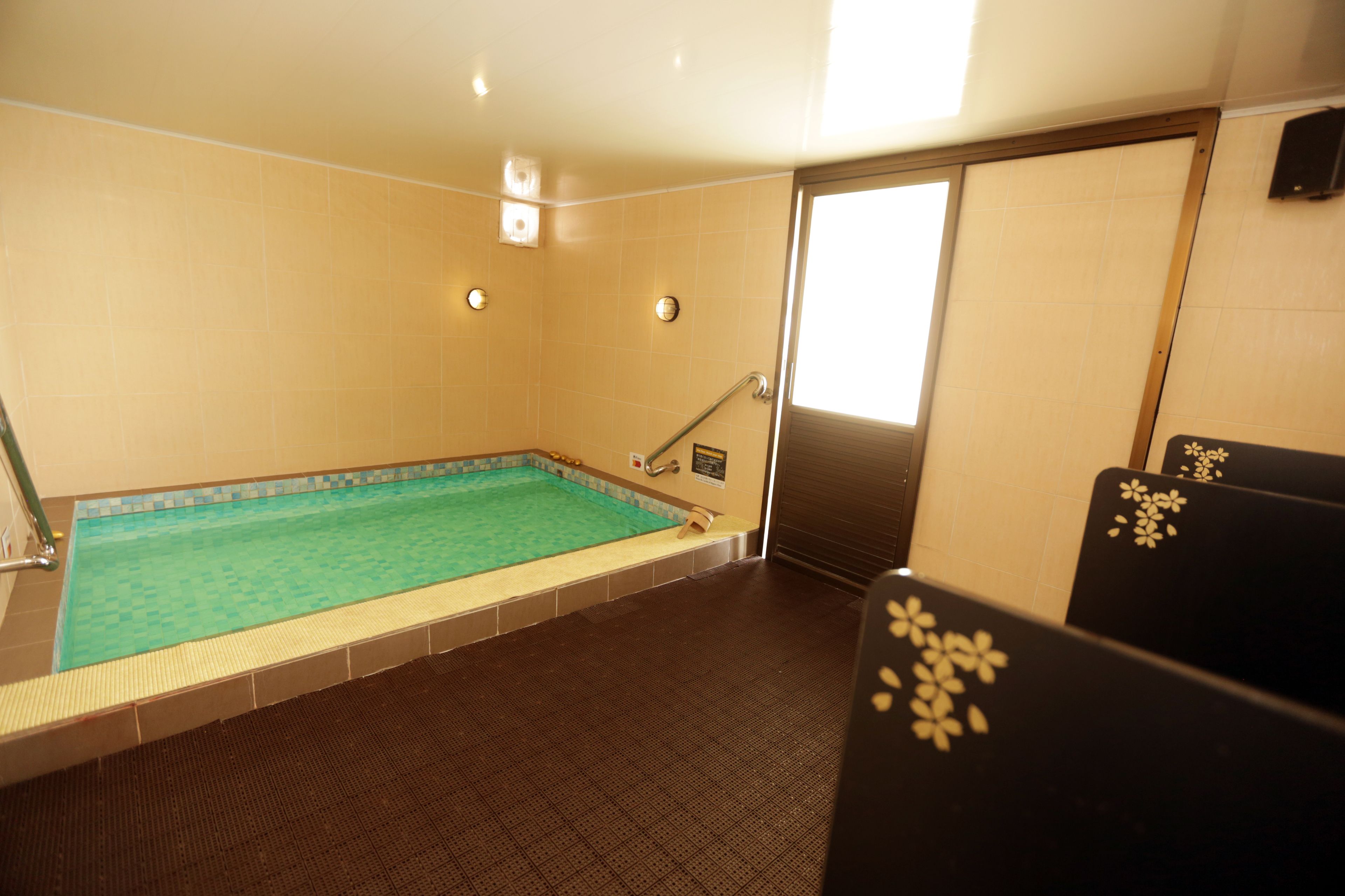 A small indoor pool with a tiled floor, a metal ladder, and a door leading to another room.
