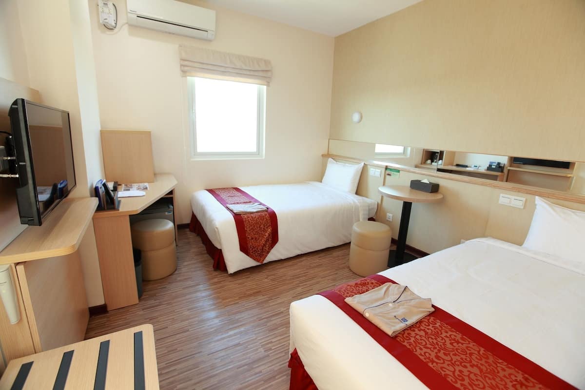 Ein Hotelzimmer mit zwei Betten, einem Schreibtisch mit Fernseher, einem kleinen Tisch und einem Fenster mit Blick.