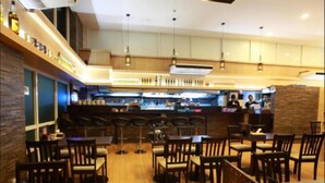 A restaurant with wooden furniture, a bar area, and a kitchen in the background. - Super Hotel Yangon Kabar Aye Road (Yangon)