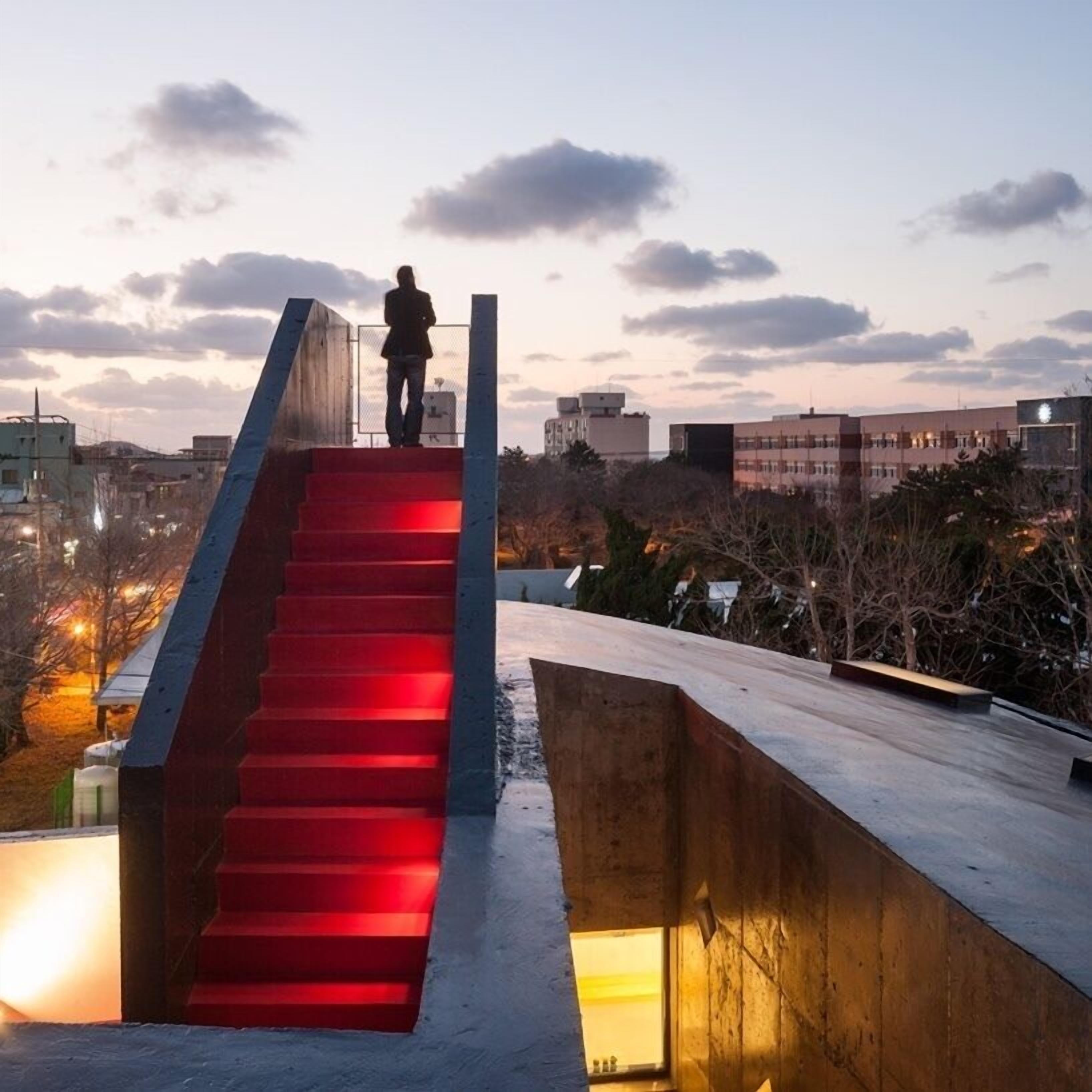 A staircase with red lighting leading to a platform, surrounded by buildings and trees.