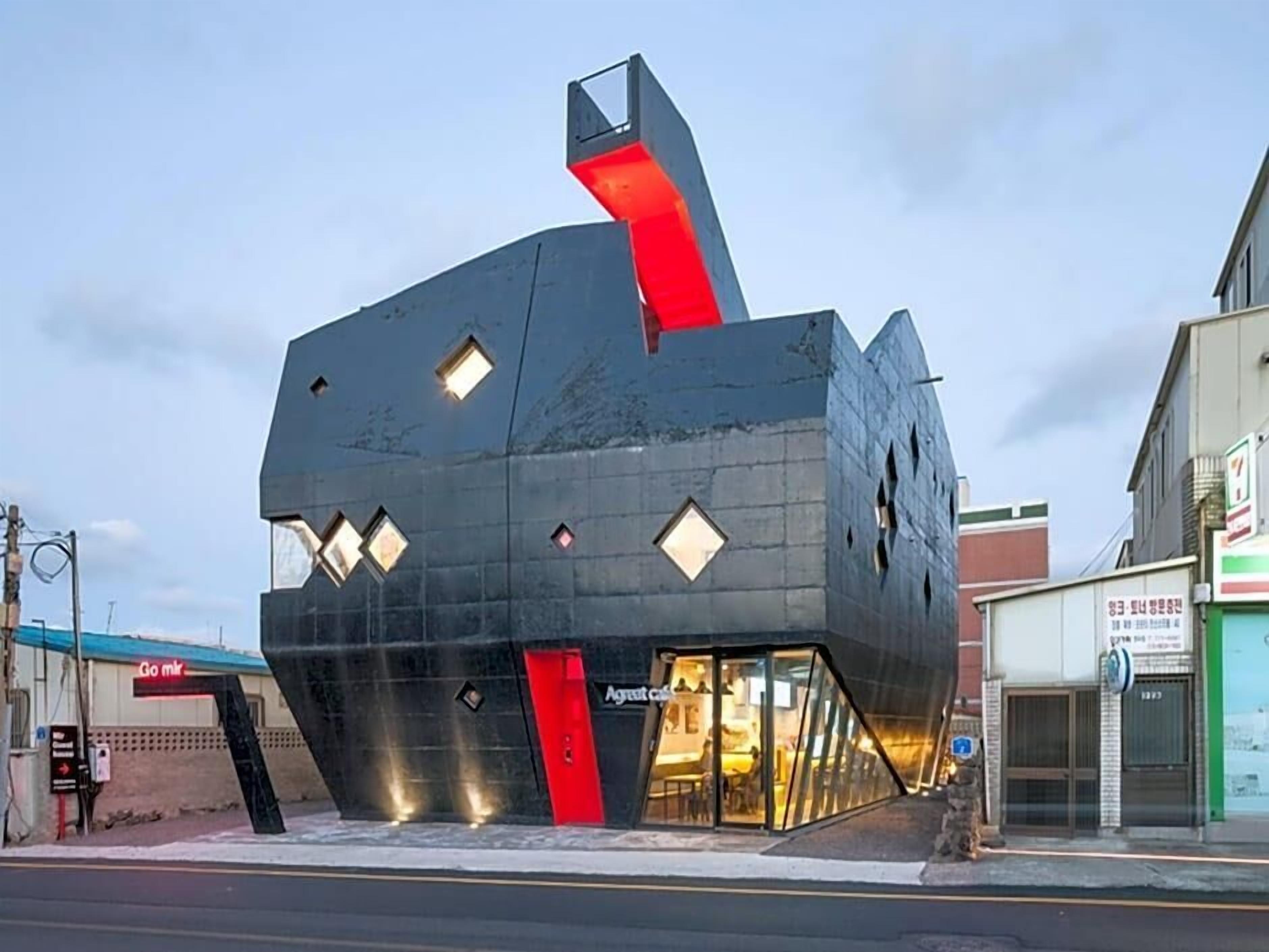 A modern building with a unique angular design, featuring a prominent red vertical element and multiple windows.