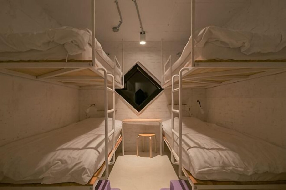 A dormitory room with bunk beds, a small window, and a desk.