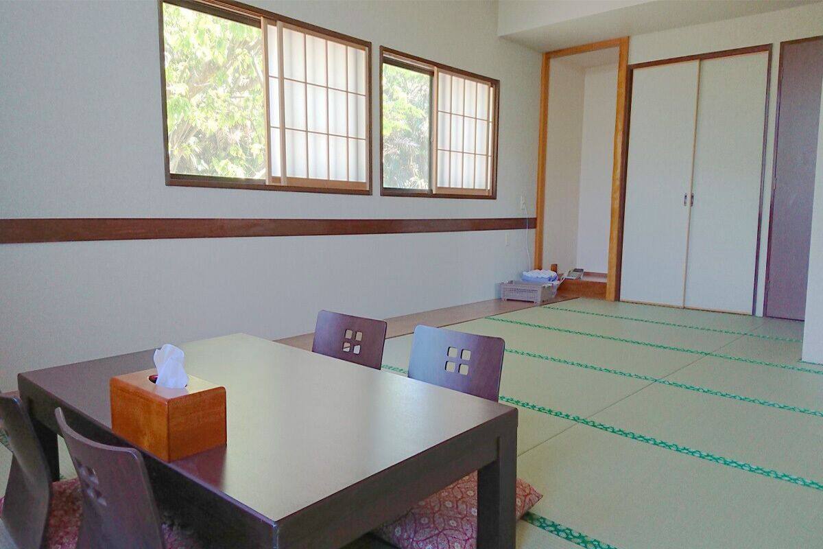 Een traditionele Japanse kamer met tatami vloermatten, een houten tafel met stoelen en glijdende deuren.