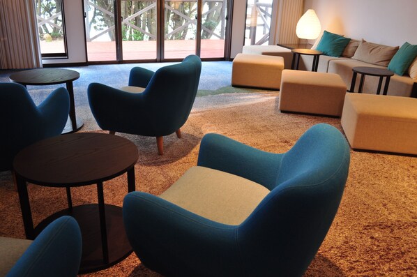Un área de estar moderna con sillones azules, un sofá color beige y una pequeña mesa.