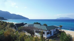Ein Küstenanwesen mit Blick auf den Strand, ein kleines Haus und ein Berg im Hintergrund.