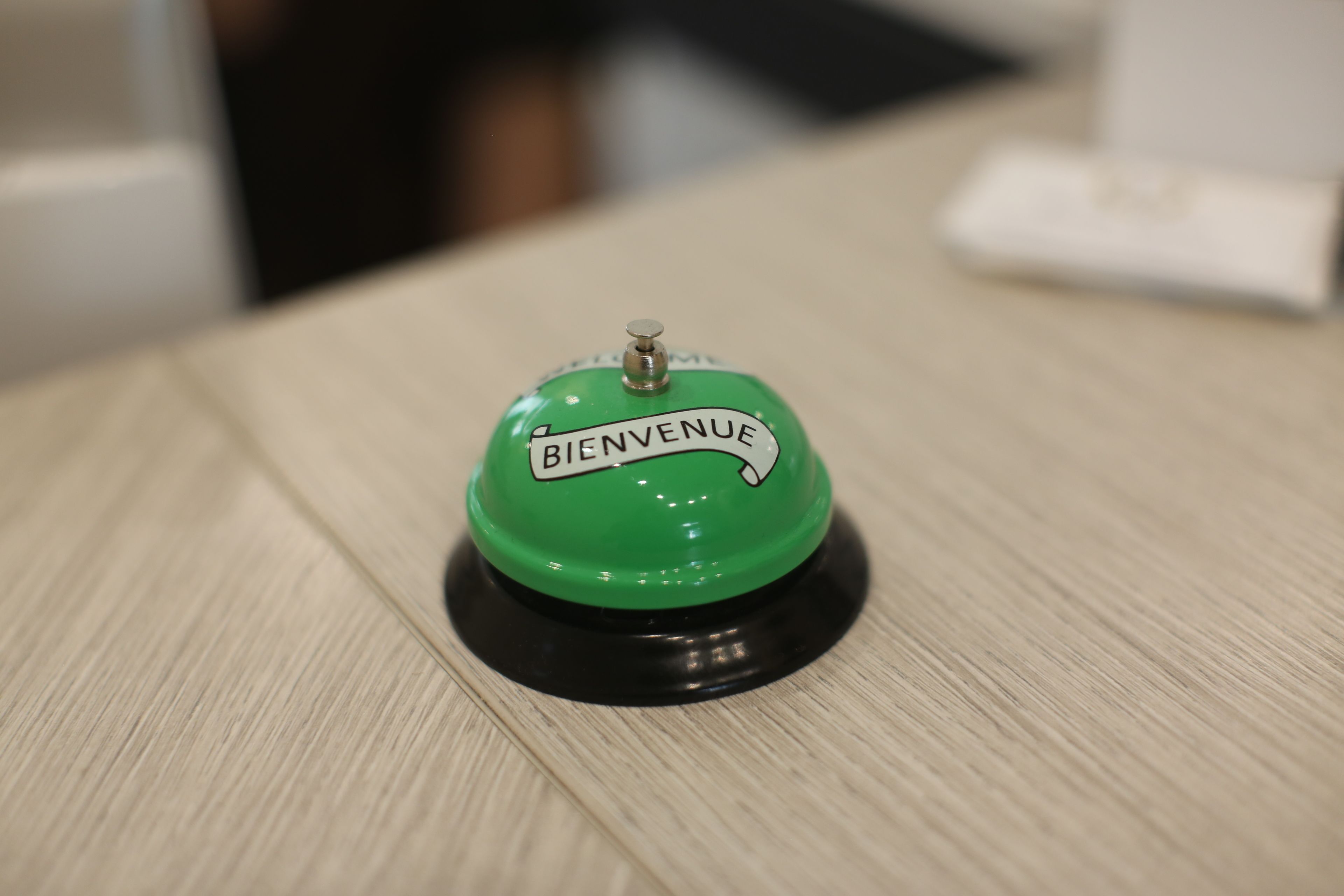 A green button with "BIENVENUE" text on a wooden surface.