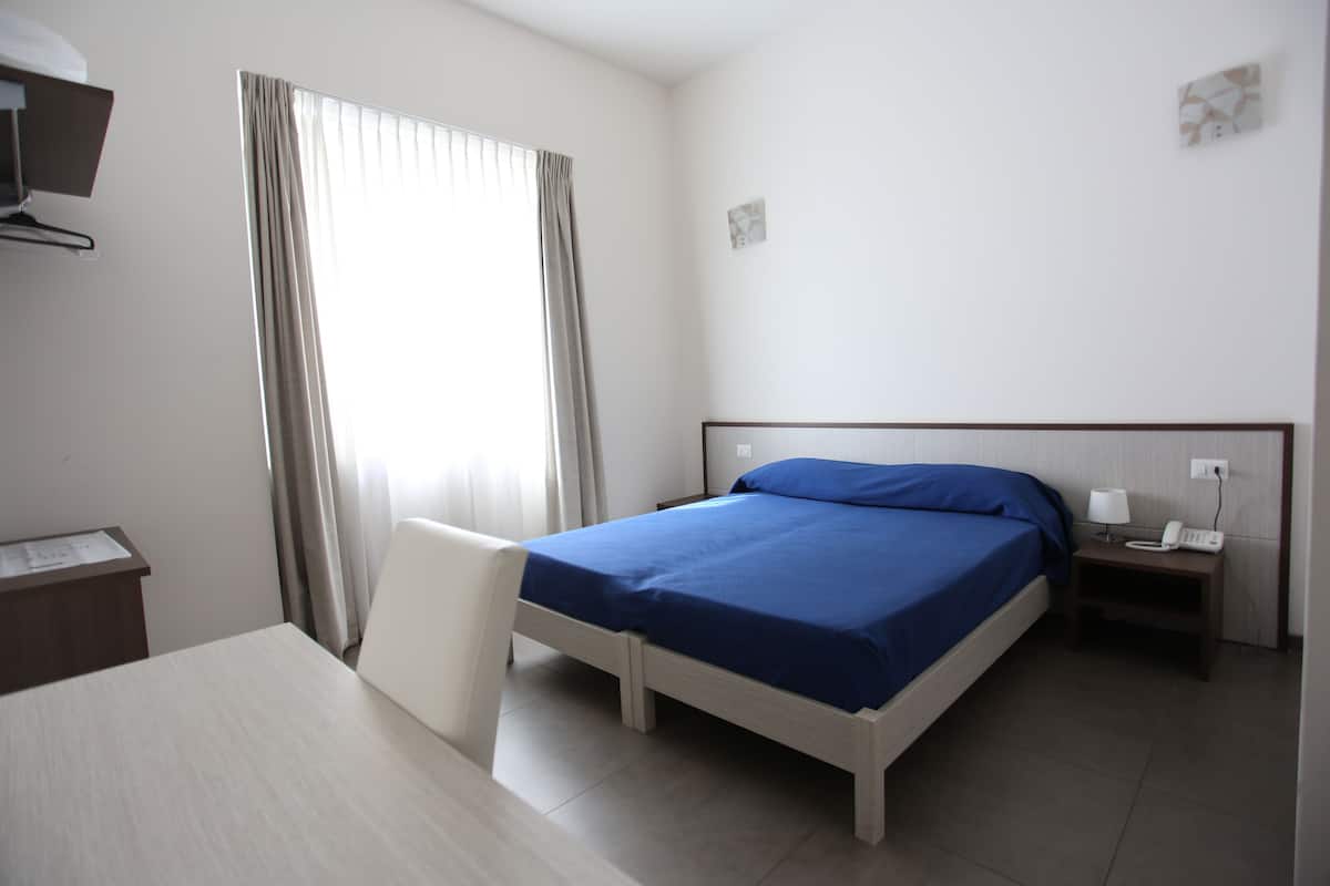 Habitación de hotel con cama, escritorio, silla, mesita de noche y ventana con cortinas.