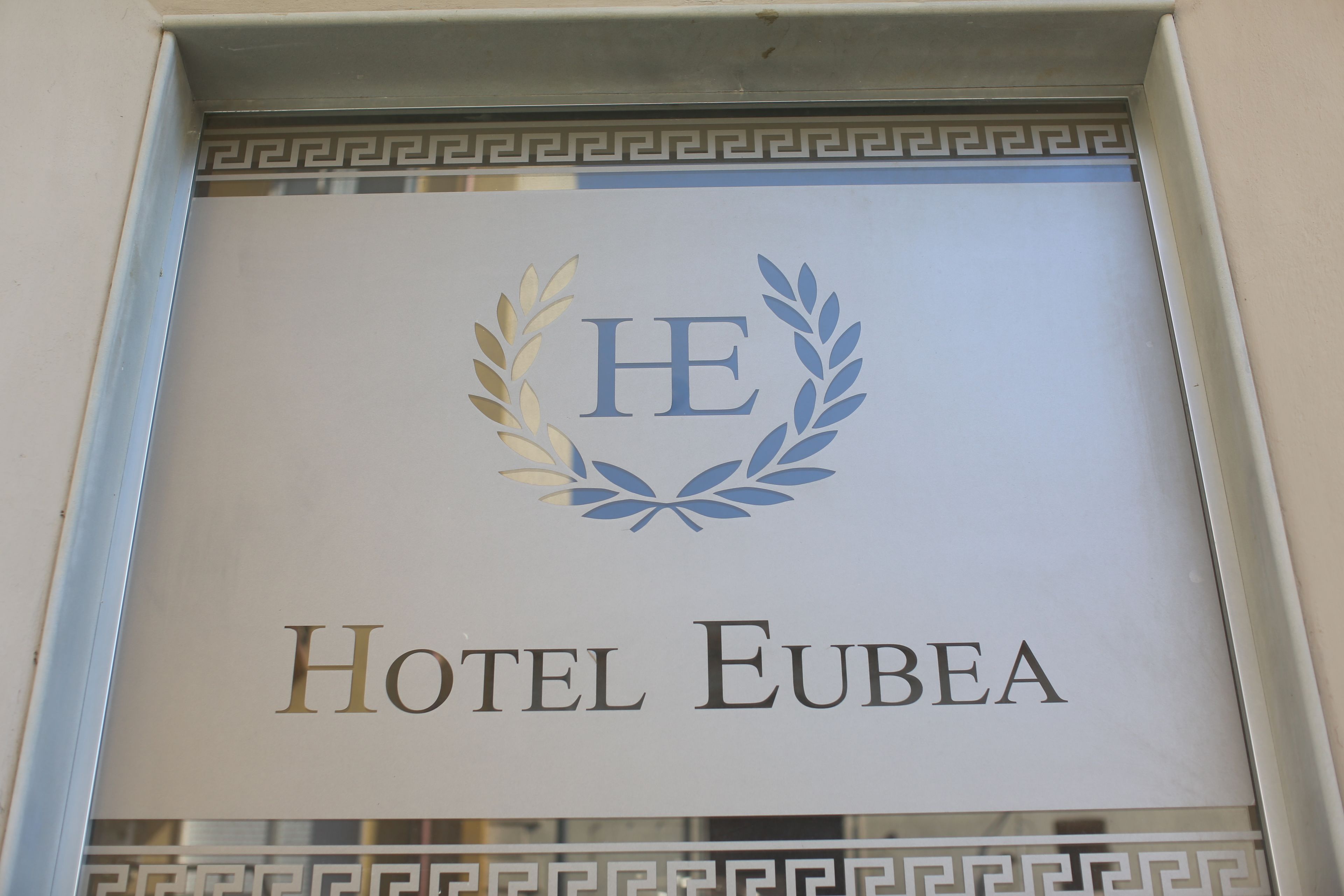 A sign for Hotel Eubea with a laurel wreath and the letters "HE" in the center.
