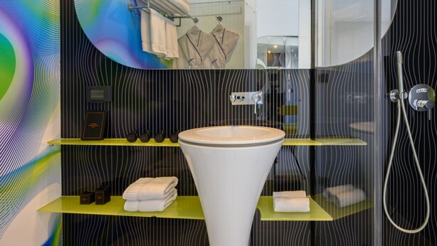 Ein modernes Badezimmer mit Waschbecken, Dusche und Spiegel. Handtücher und Pflegeprodukte befinden sich in Regalen.