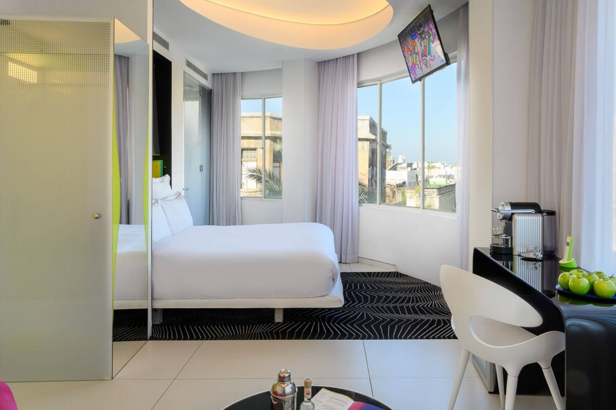 Une chambre d’hôtel moderne équipée d’un lit, d’un bureau avec un ordinateur portable, d’une chaise et offrant une vue sur la ville.