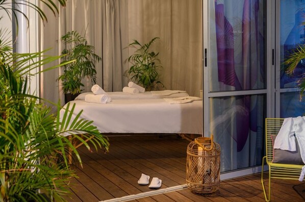 Une chambre d’hôtel avec un lit, une grande fenêtre avec des rideaux, un panier en osier et une chaise jaune.