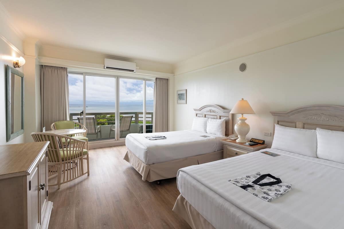 Een hotelkamer met twee bedden, een bureau, een stoel en uitzicht op de oceaan.