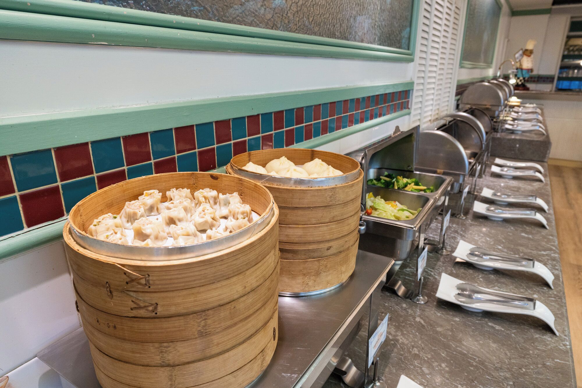 A buffet setup with bamboo steamers filled with dumplings and a variety of dishes in metal containers.