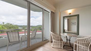 A balcony with a view of a red-roofed building and greenery, wicker chairs, a small round table, and a wall-mounted mirror.