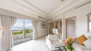 Een ruime woonkamer met een witte bank, een glazen salontafel en uitzicht op de oceaan door grote schuifdeuren.