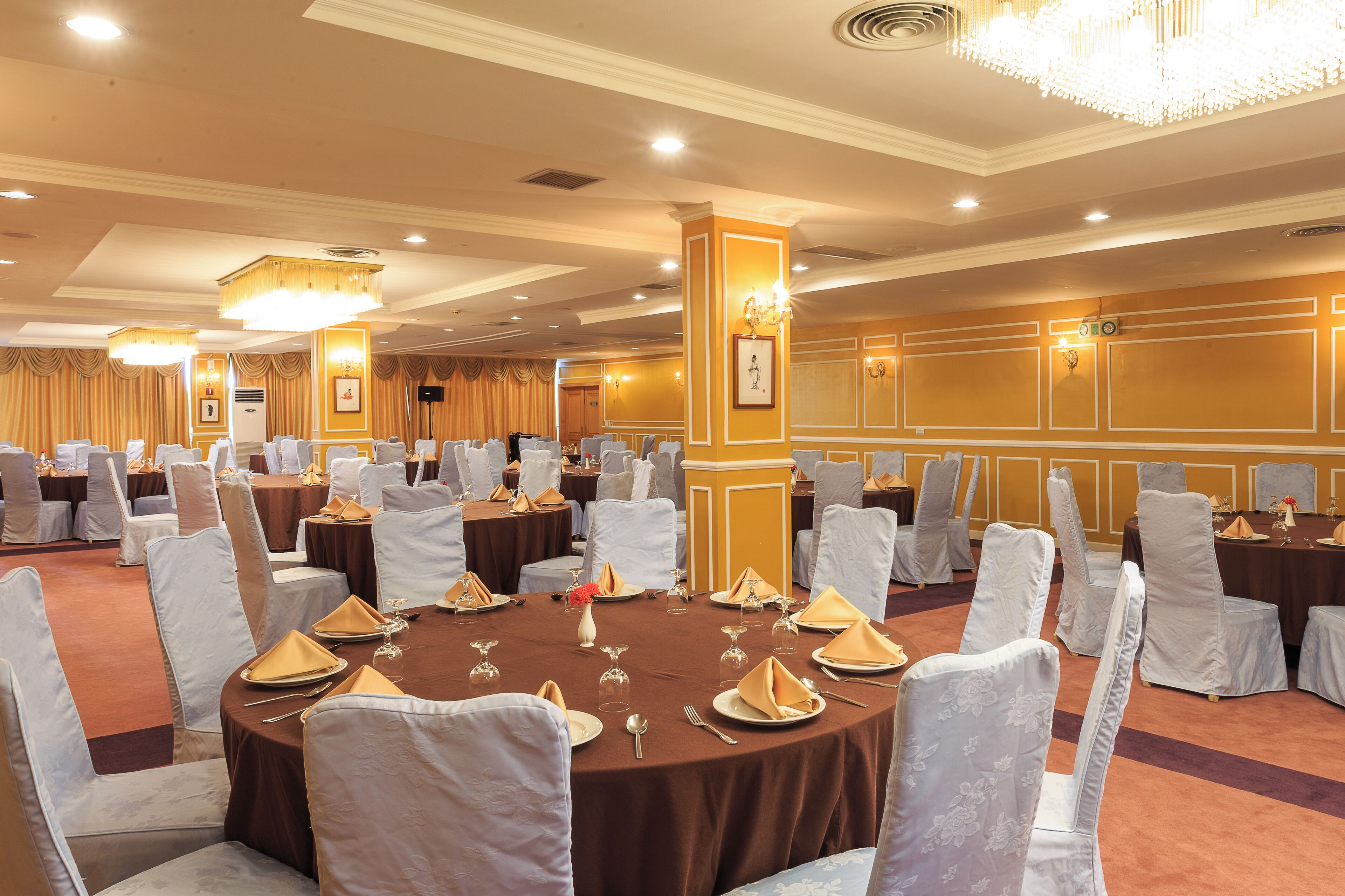 Un salón de banquetes con mesas redondas, sillas blancas y candelabros.