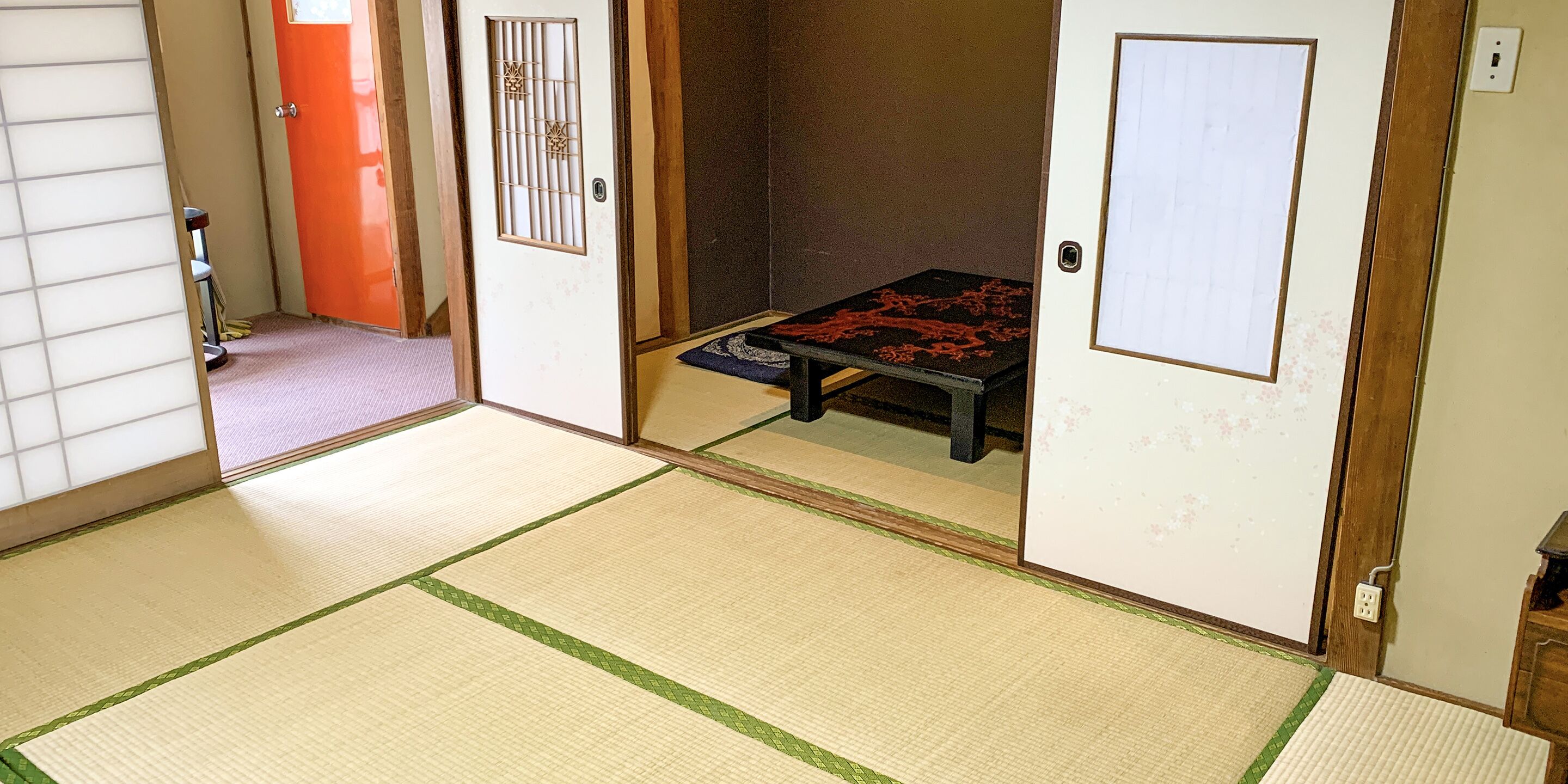 A traditional Japanese room with tatami flooring, a low table with a red and black patterned mat, and sliding doors.