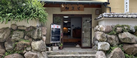 A traditional Japanese building with a stone entrance, a wooden signboard, and a tiled roof.