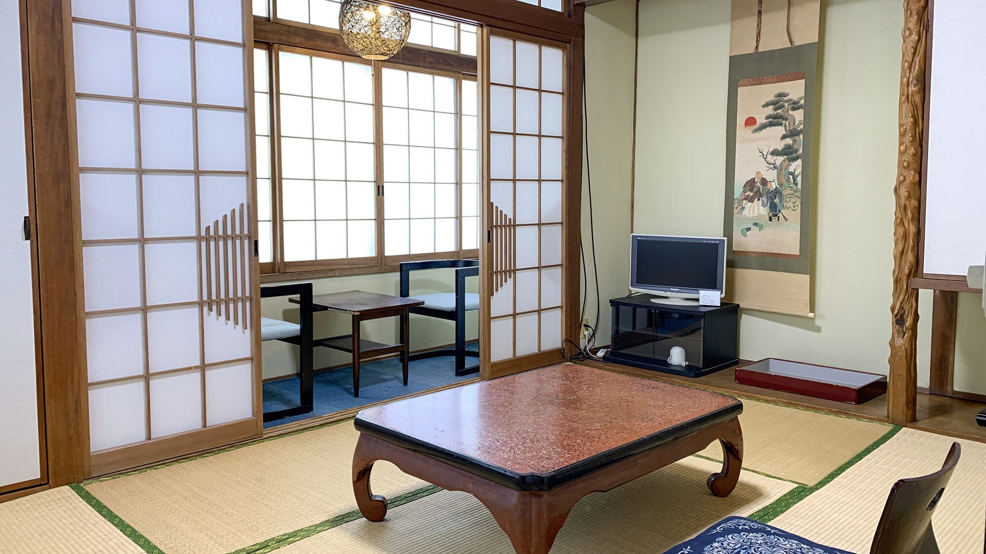 A traditional Japanese room with tatami flooring, a low table, a television on a stand, and sliding doors.
