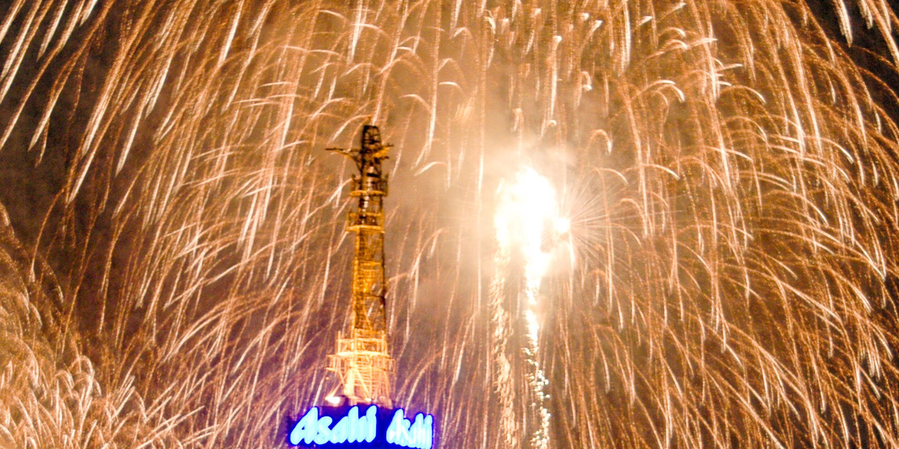 Una torre con un letrero iluminado en la base, rodeada de fuegos artificiales.