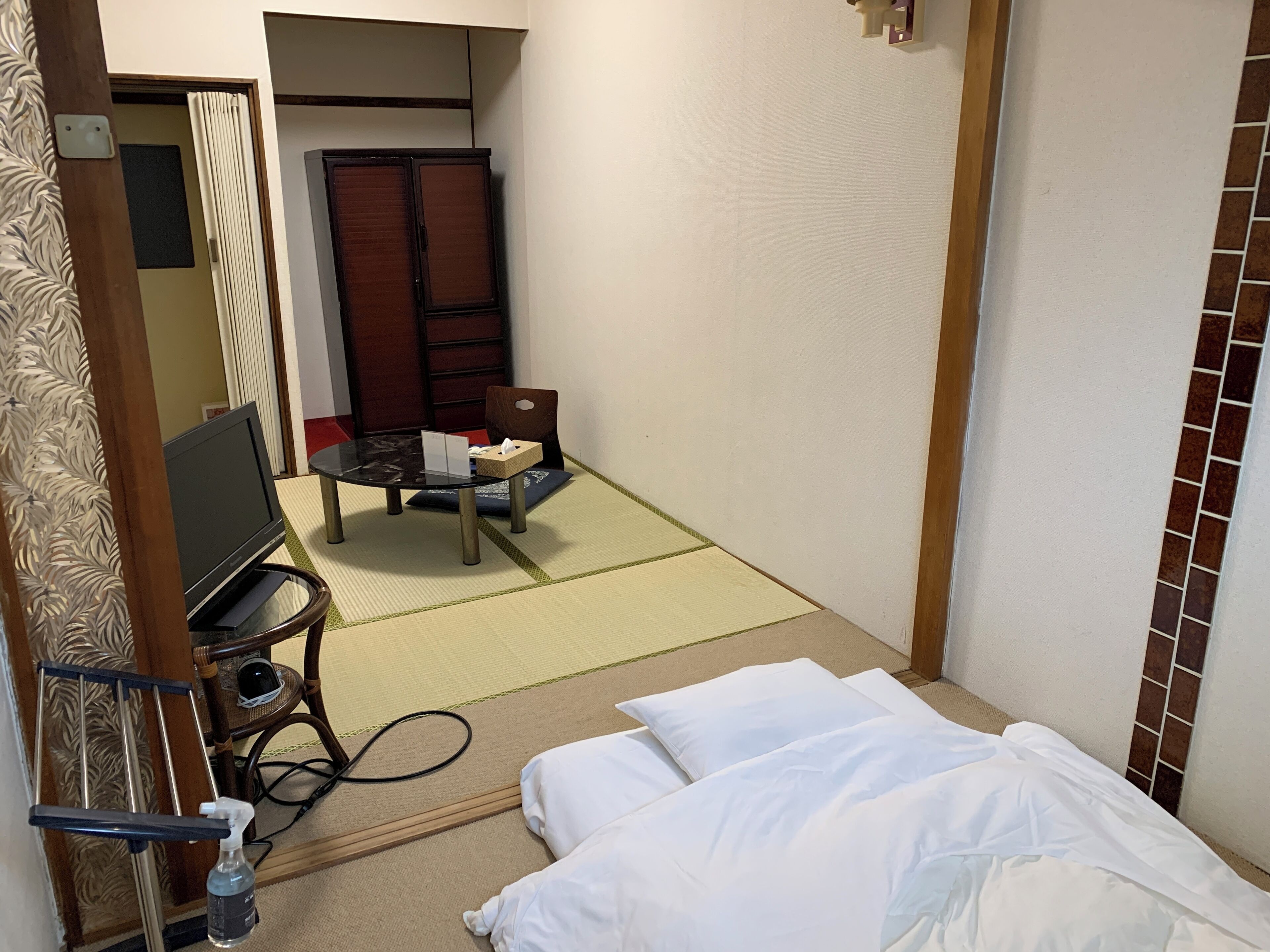 A hotel room with a bed, a desk with a chair, a television, and a small table with a tissue box.
