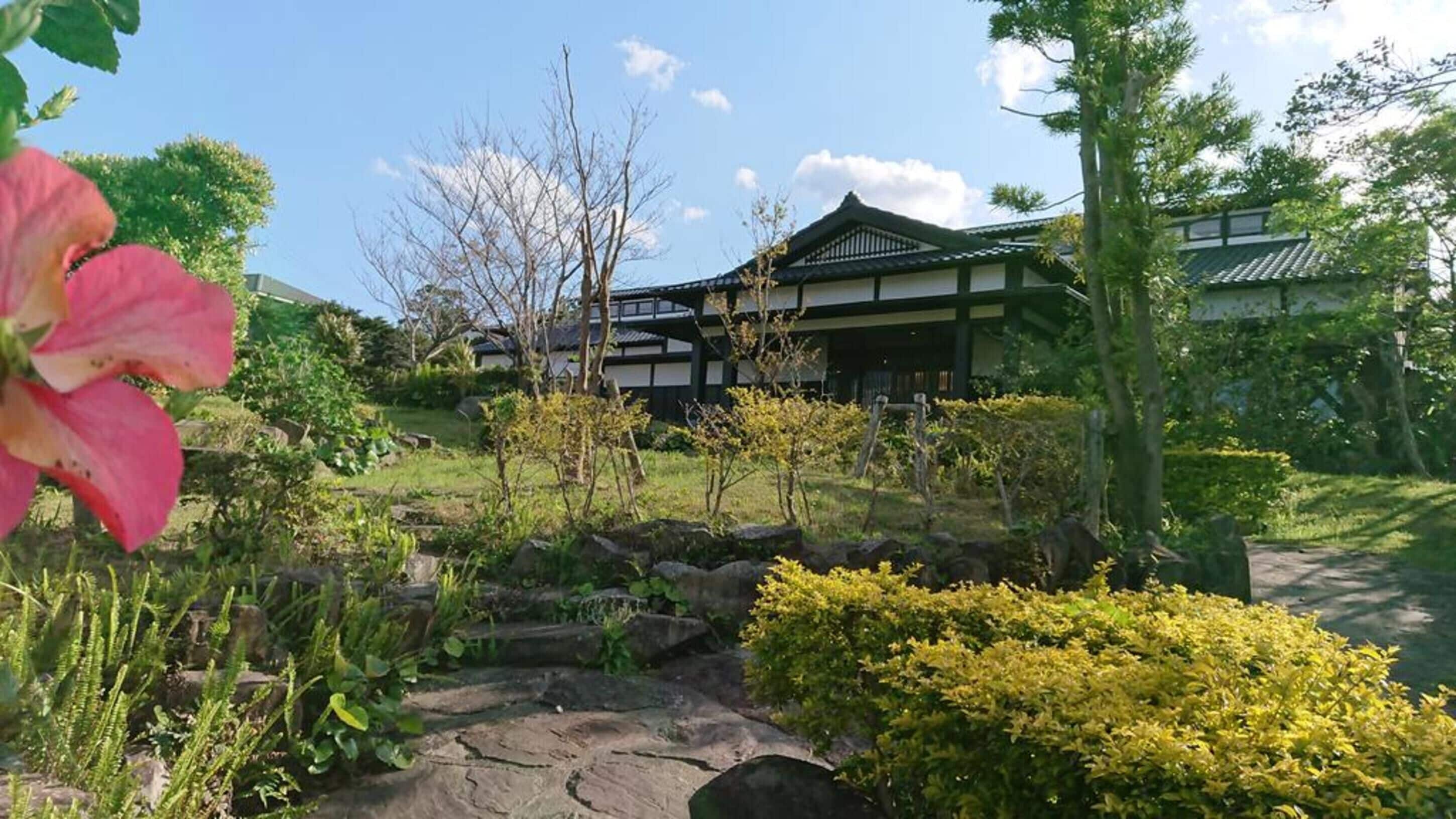 A traditional Japanese building with a tiled roof, surrounded by a garden with rocks and shrubs.