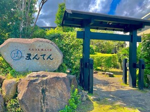 A stone sign with Japanese characters, a wooden structure, and a pathway surrounded by greenery. - Yakushima Jomon No Yado Manten (Yakushima)