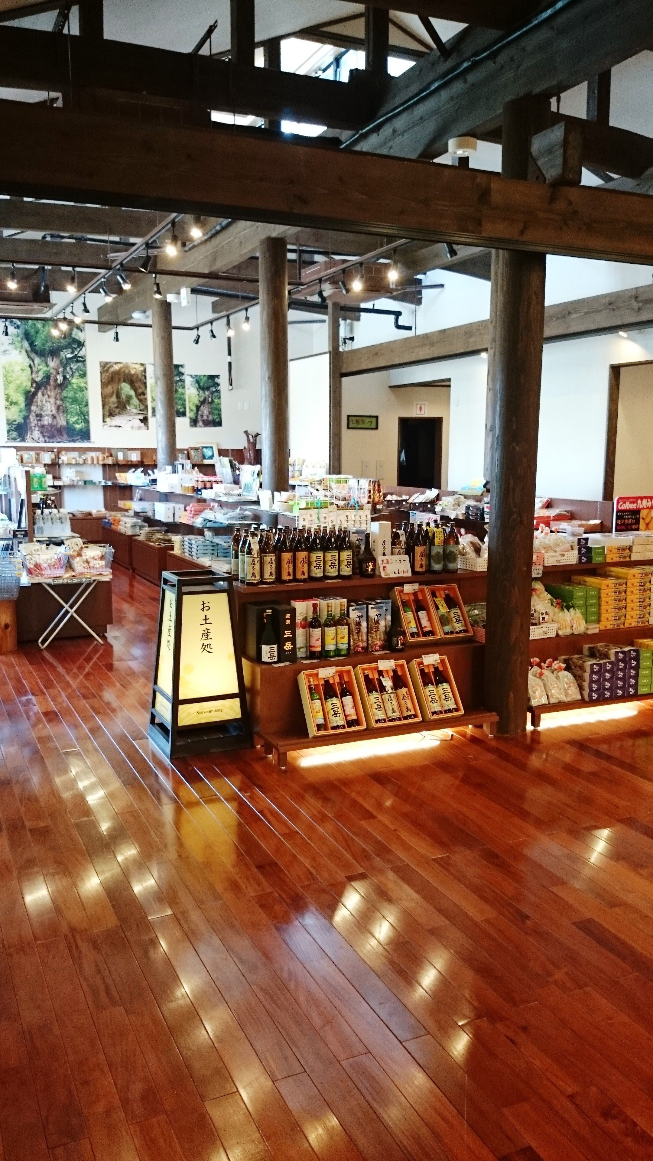 A spacious store with wooden floors and high ceilings, featuring shelves stocked with various products and a display area for items.