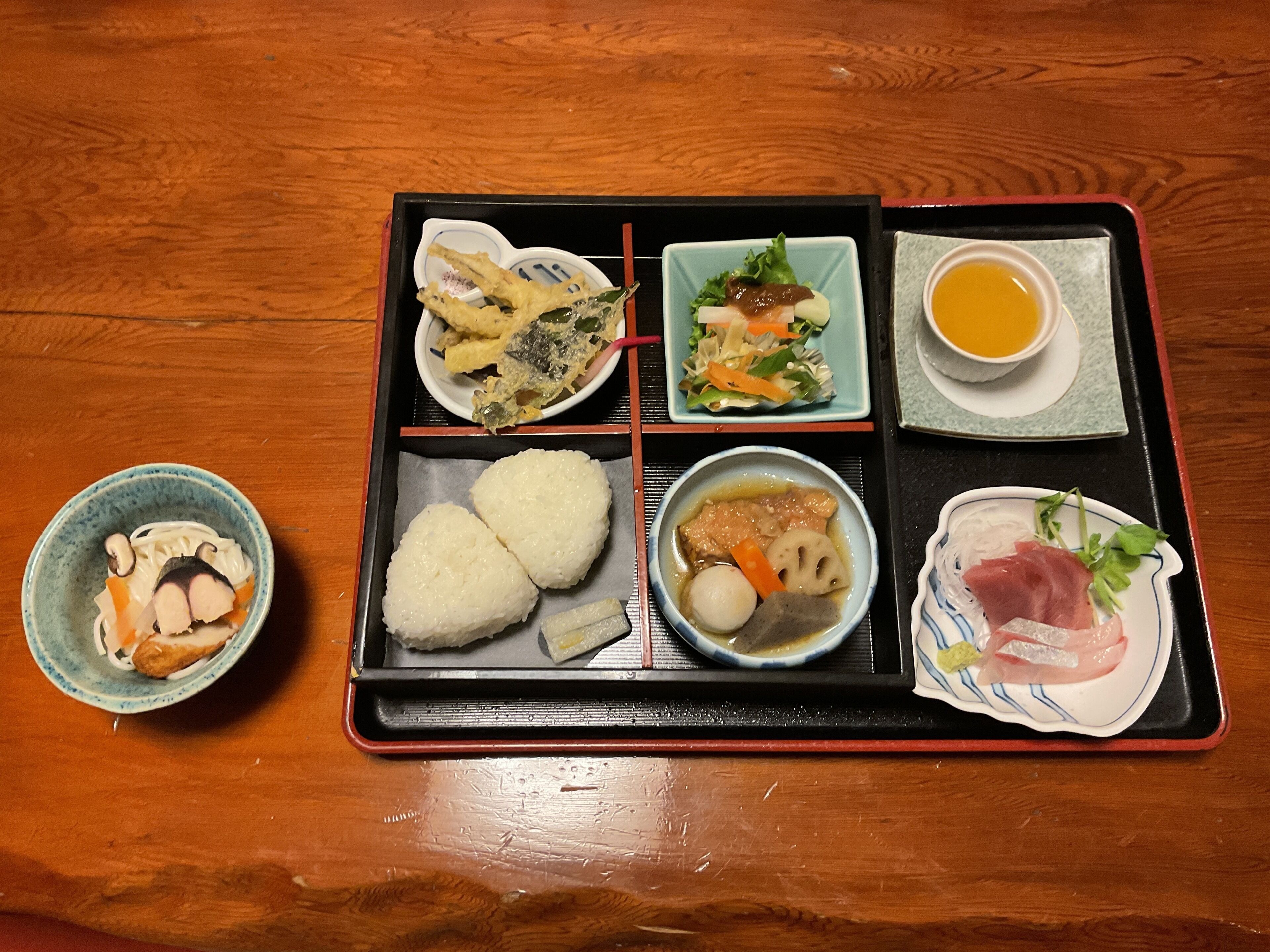 A tray with various Japanese dishes including tempura, salad, soup, and sashimi.