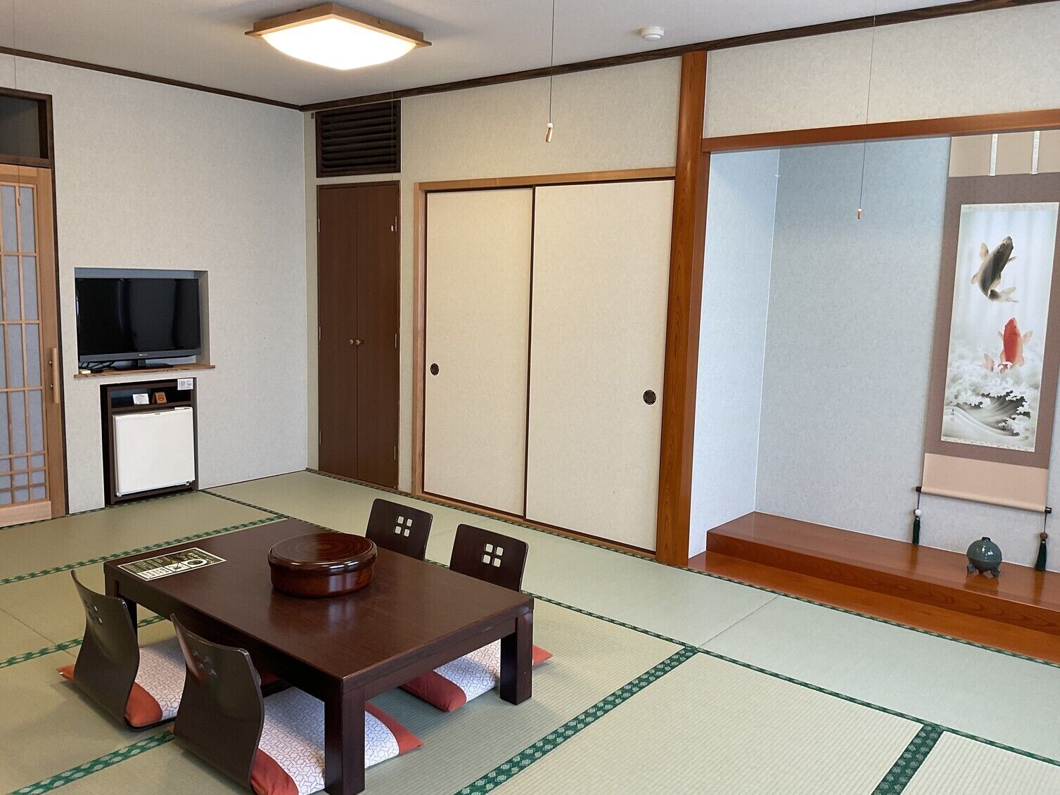 A traditional Japanese room with tatami flooring, a low table with cushions, a television, and sliding doors.