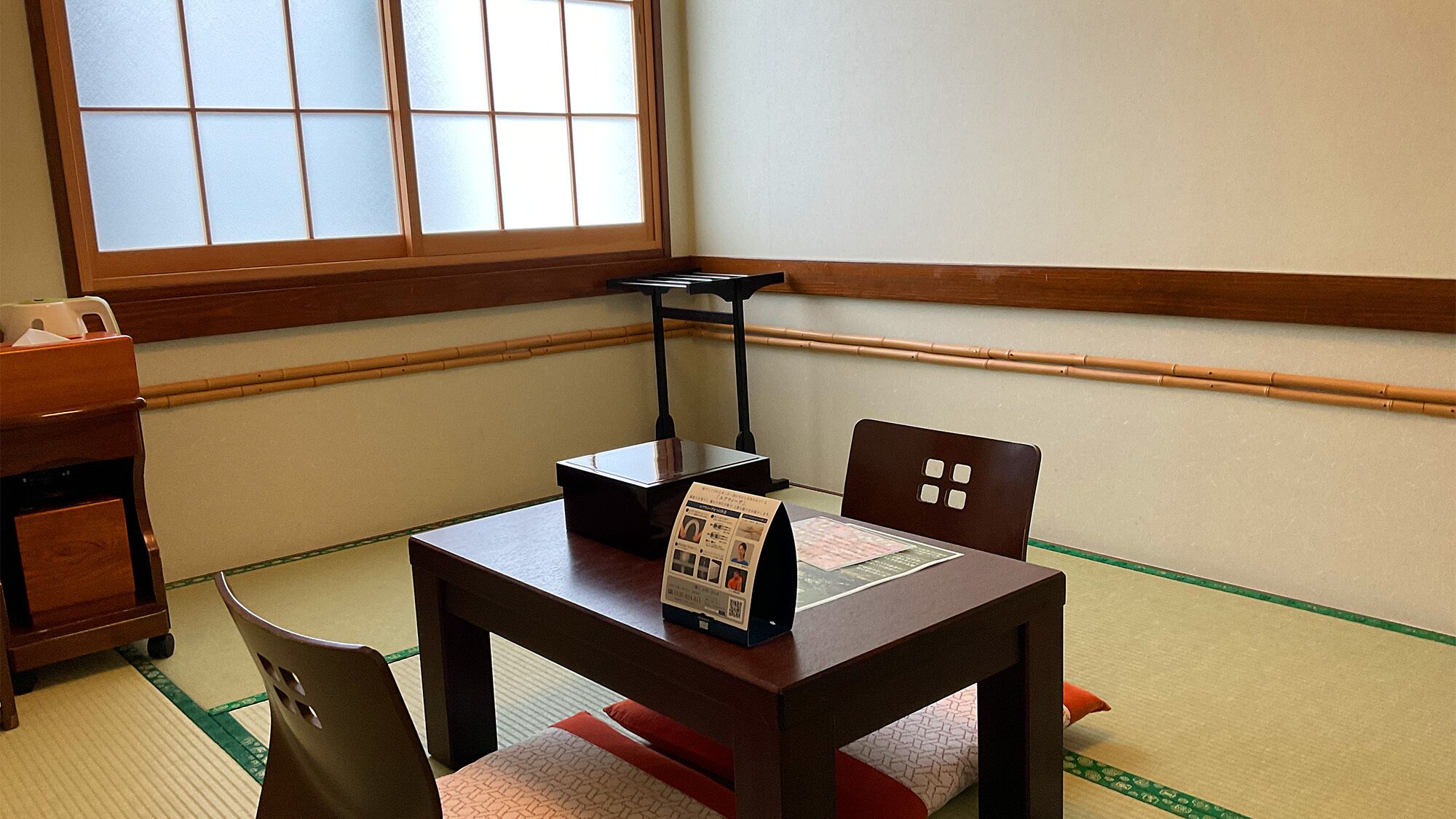 A traditional Japanese room with tatami flooring, a low table with a black tray, a wooden chair, and a window with frosted glass.
